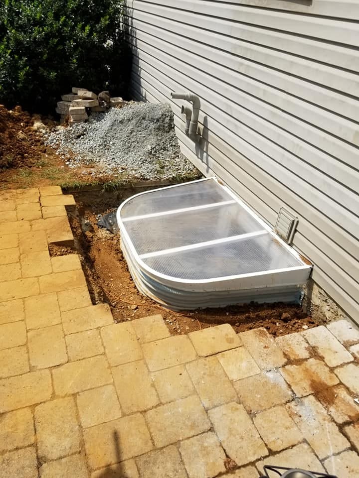 New egress window well installed against a house foundation with paver walkway