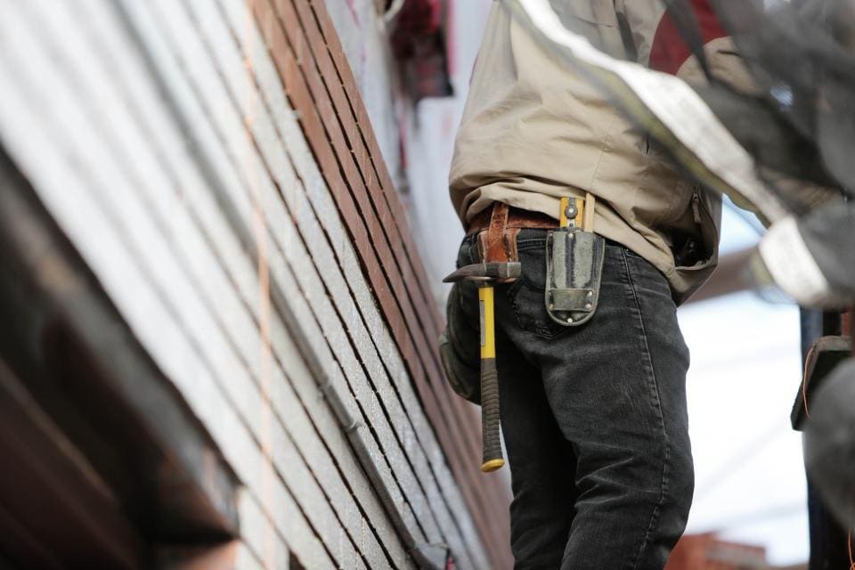 Carpenter with a tool belt and hammer working on a wood wall